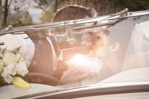 Recién casada pareja besándose en vintage coche — Foto de Stock