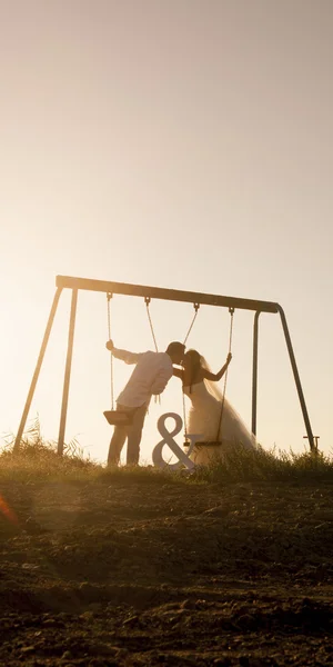 Couple nouvellement marié embrasser sur les balançoires — Photo