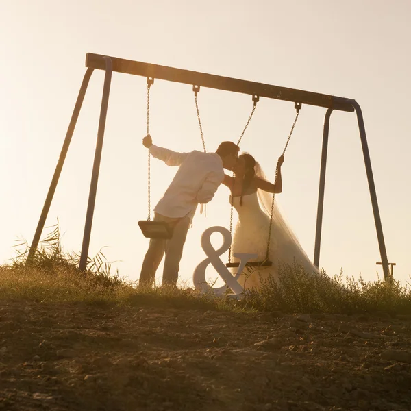 Couple nouvellement marié embrasser sur les balançoires — Photo