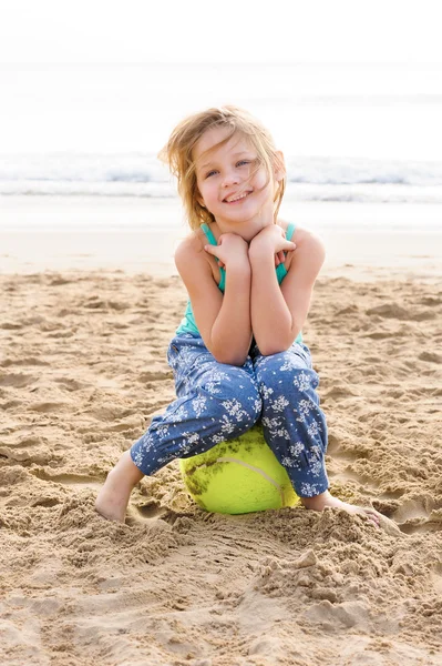 Meisje zittend op een bal op strand — Stockfoto