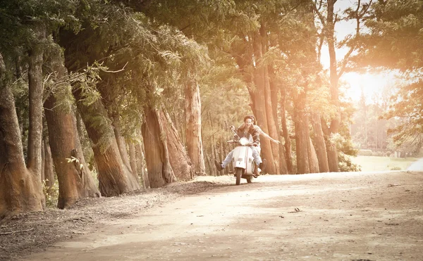 Young happy couple traveling by scooter along dirt road — Stock Photo, Image