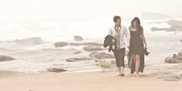 Atractiva pareja joven caminando por la playa a través de la niebla —  Fotos de Stock