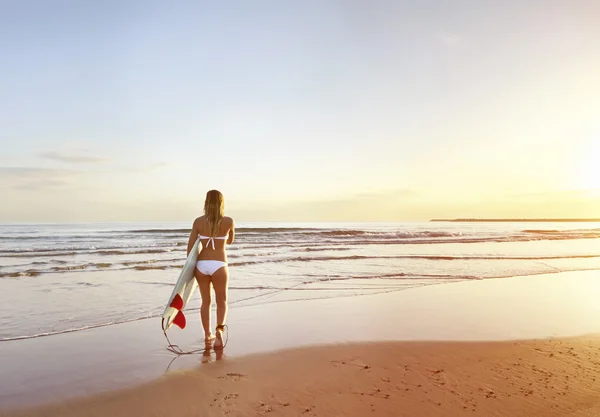 Menina surfista atraente jovem na praia com prancha ao nascer do sol — Fotografia de Stock