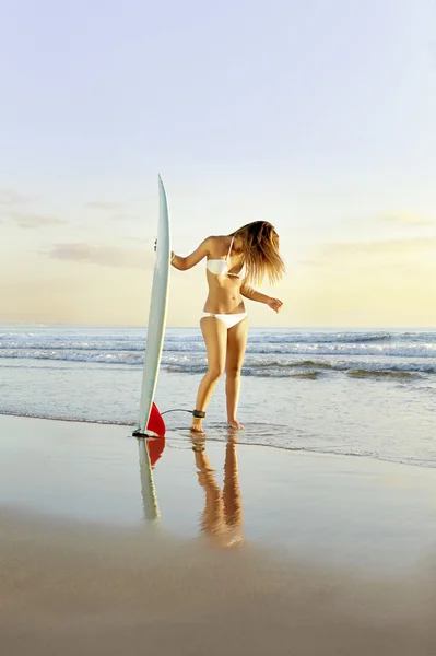 Молода приваблива дівчина-серфер на пляжі з дошкою для серфінгу на сході сонця — стокове фото