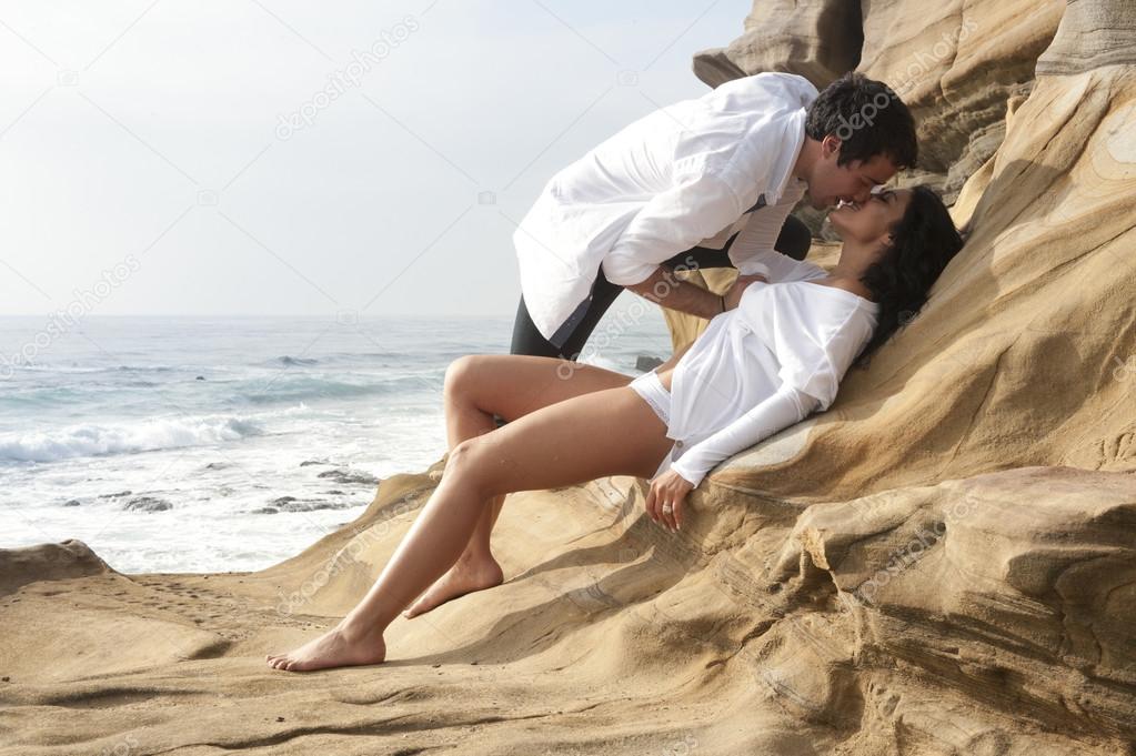 Attractive in love couple relaxing together on rocks overlooking beach