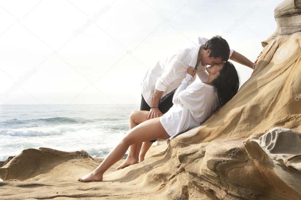 Attractive in love couple relaxing together on rocks overlooking beach