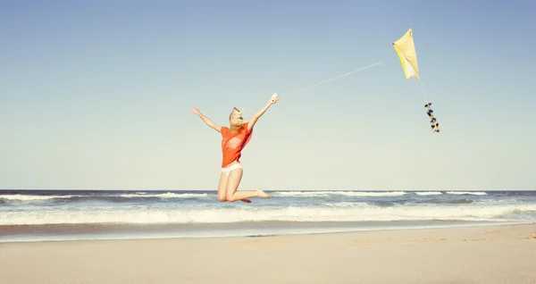 Ung, attraktiv jente som flyr gul drage på stranden i bikini – stockfoto