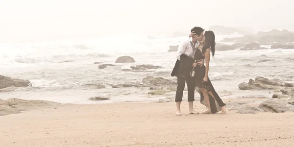 Felice coppia attraente flirtare sulle rocce della spiaggia sotto cieli nuvolosi — Foto Stock