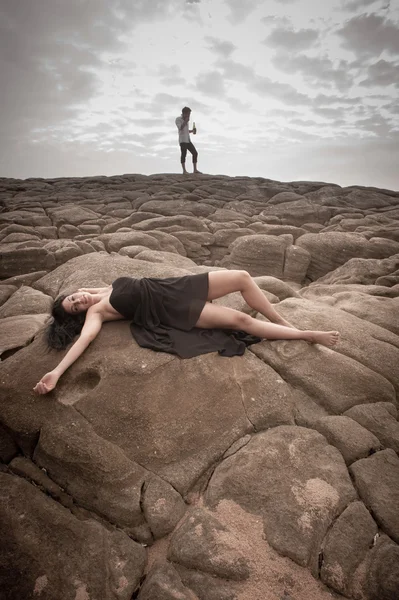 Gelukkige aantrekkelijke paar flirten op strand rotsen onder wolkenluchten — Stockfoto