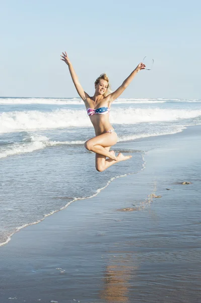 Aantrekkelijke blonde meisje springen op het strand in bikini — Stockfoto