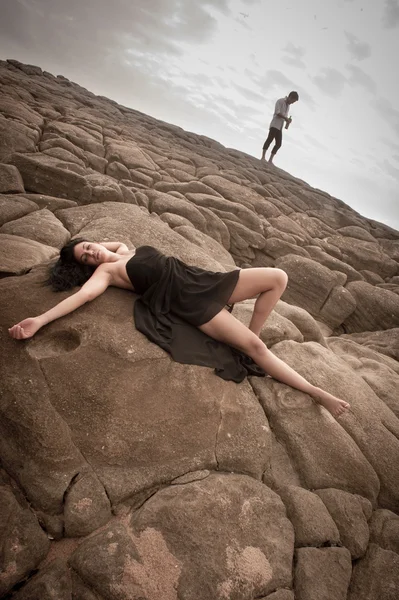 Feliz pareja atractiva coqueteando en rocas de playa bajo cielos nublados — Foto de Stock