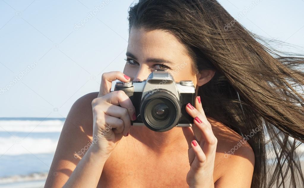 Young attractive girl taking photos with camera at the beach