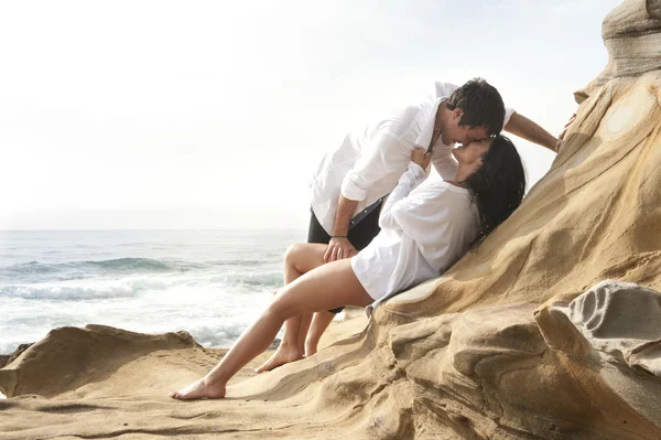 Jonge aantrekkelijke paar ontspannen samen op de rotsen bij strand zoenen en flirten — Stockfoto