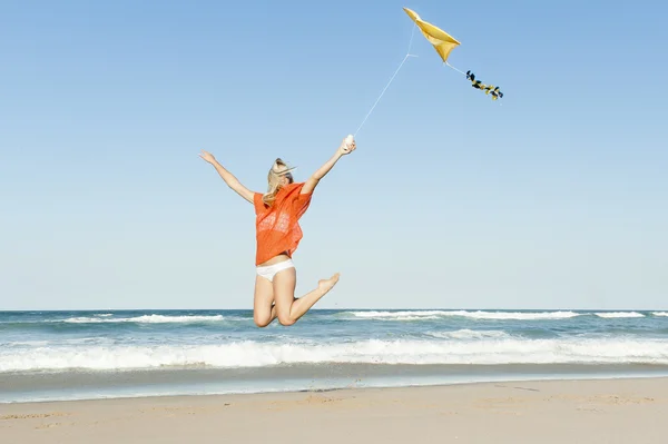 Joven chica feliz saltando en la playa con cometa amarilla —  Fotos de Stock