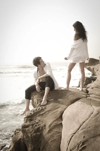 Jonge aantrekkelijke paar ontspannen samen op de rotsen bij strand zoenen en flirten — Stockfoto