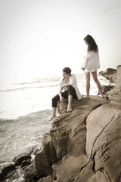 Joven pareja atractiva relajándose juntos en las rocas en la playa besando y coqueteando — Foto de Stock