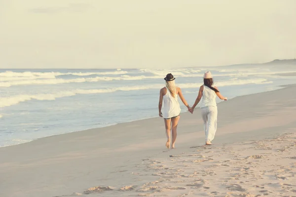Две молодые привлекательные лесбиянки идут вдоль пляжа, держась за руки — стоковое фото
