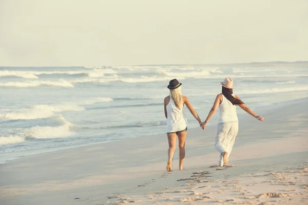 Dwie młode atrakcyjne lesbijki dziewczyny spaceru wzdłuż plaży trzymając się za ręce — Zdjęcie stockowe