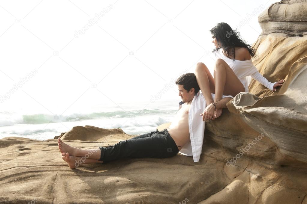Young attractive couple relaxing together on rocks at beach kissing and flirting