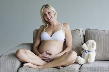 Genç hamile kadın bir oyuncak ayı ile kanepede rahatlatıcı
