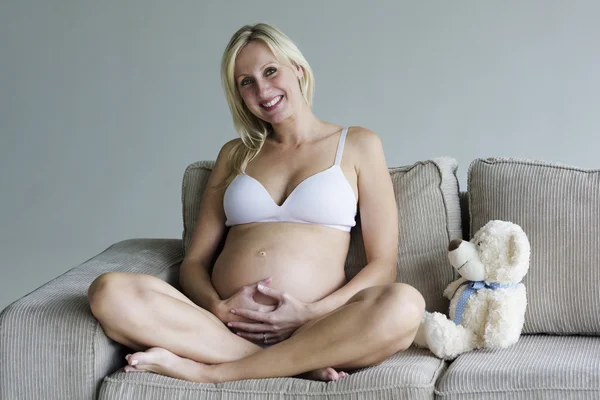 Jovem grávida relaxando no sofá com um ursinho de pelúcia — Fotografia de Stock