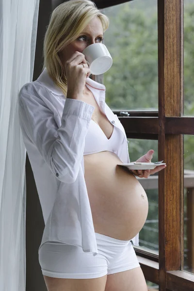 Mujer embarazada joven disfrutando de una taza de té en la ventana — Foto de Stock