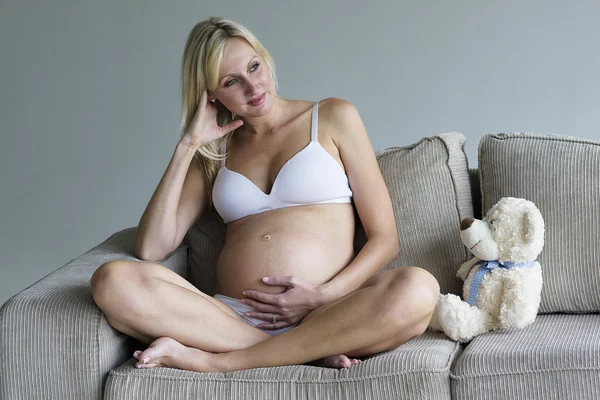 Jovem grávida relaxando no sofá com um ursinho de pelúcia — Fotografia de Stock