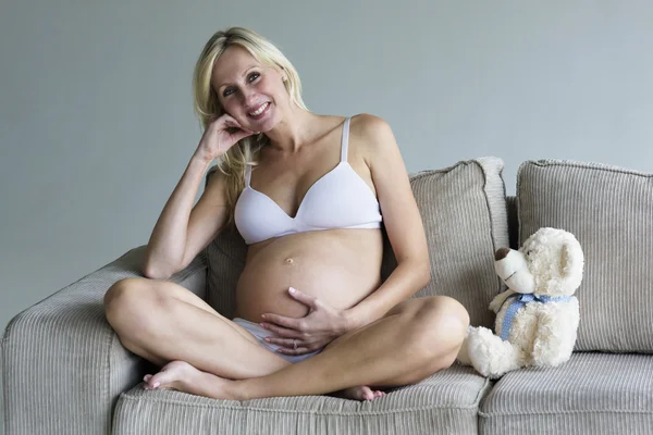 Mujer embarazada joven relajándose en el sofá con un oso de peluche — Foto de Stock