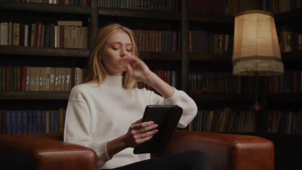 Junge Frau fixiert ihre Haare, während sie zu Hause ein Tablet liest — Stockvideo