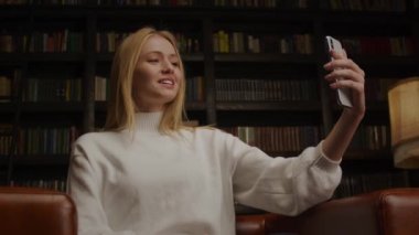 Gülümseyen 20 'li yaşlarda, sarışın, beyaz bir kadın telefonda arkadaşlarıyla zumluyor.