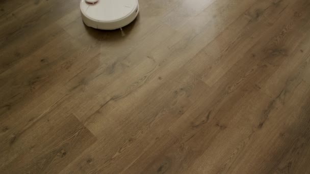 Белый робот-пылесос чистит деревянный пол — стоковое видео
