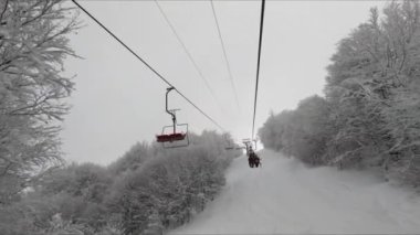 Bulutlu bir günde ağaçlarla kaplı bir sandalyede yükselirken, sandalyeler yanından geçiyor.