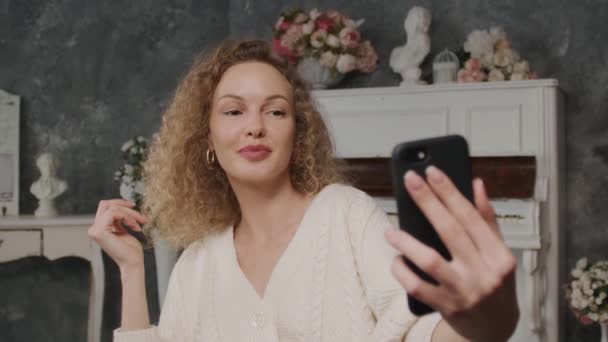 Eine junge Frau in den 30er Jahren macht ein Selfie mit einem Smartphone und posiert vor einer Handykamera — Stockvideo