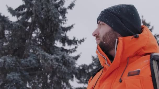 Веселый 30-летний мужчина, оглядывающийся вокруг и улыбающийся в снежный зимний день на улице — стоковое видео