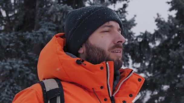 Кавказский мужчина идет к камере под соснами, покрытыми снегом — стоковое видео
