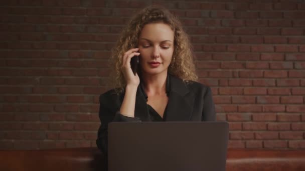 Die geschäftige junge erwachsene blondgelockte Geschäftsfrau aus den 30er Jahren telefoniert in einer Loft-Wohnung mit einem modernen Laptop — Stockvideo