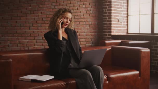 Rušné mladé dospělé kudrnaté blond 30s podnikatelka mluví na telefonu v podkrovním bytě s moderním notebookem — Stock video