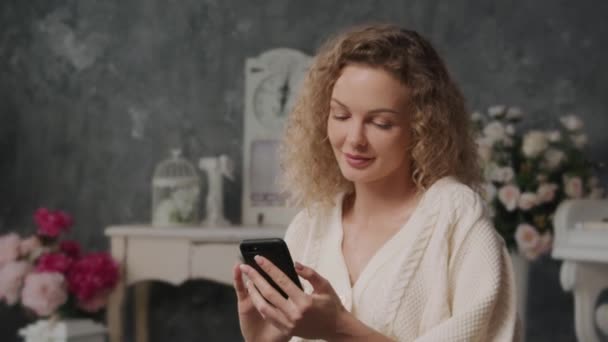 Una persona de 30 años joven caucásica rubia mujer tímida mensajes de texto en su teléfono y sonriendo sensualmente — Vídeos de Stock