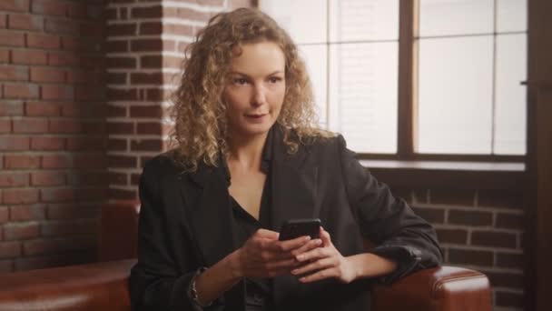Молода бізнес-леді 30 років невизначена - думає і типи і відповідає на смартфон в квартирі на горищі — стокове відео