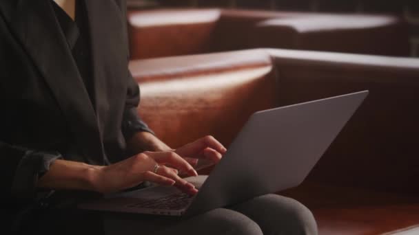 Mujer irreconocible vestida con un traje moderno sentada en un sofá de cuero y escribiendo — Vídeo de stock