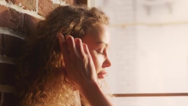 Close-up van een jonge vrouw het openen van haar ogen met een echt helder zon raken haar gezicht terwijl zitten op een raam — Stockvideo