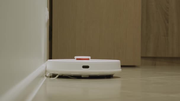 Sebuah robot pel vakum putih membersihkan lantai kayu di interior apartemen yang cerah — Stok Video