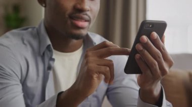 Tanımlanamayan Afro-Amerikan genç yetişkin bir adamın siyah akıllı bir telefonu aşırıp mal ararken gülümsemesi.