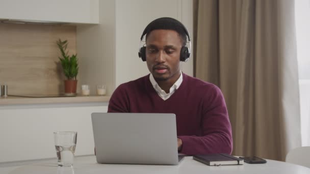 Retrato de um jovem afro-americano com auscultadores a trabalhar num portátil. Fechar de um call center emloyee trabalhando distante — Vídeo de Stock