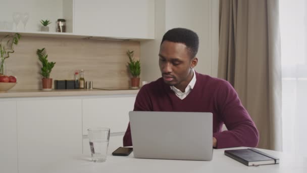 Junge 20er Jahre afrikanisch-amerikanischer schwarzer Angestellter, der einen Anruf erhält, während er zu Hause an seinem Laptop arbeitet — Stockvideo