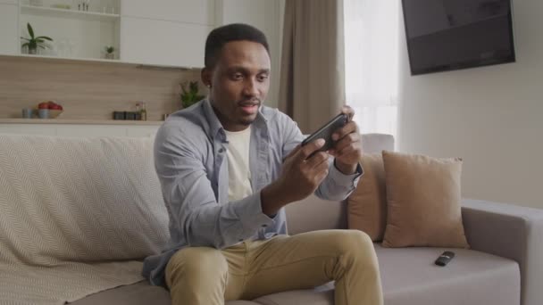 Junger erwachsener schwarzer Rüde spielt ein Spiel auf seinem Smartphone und scheitert eine Runde mit einer hellen Reaktion darauf — Stockvideo