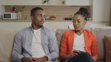 Afro-Amerikan çift bir koltukta oturup sakin bir şekilde konuşarak oturma odalarında planlarını tartışıyor.