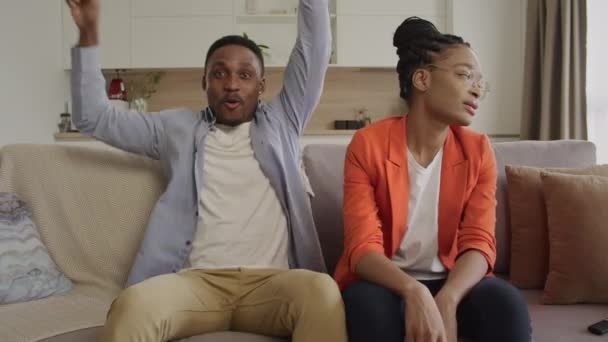 Nettes afrikanisch-amerikanisches Paar beim Konsolenspielen im heimischen Wohnzimmer. Guy gewinnt die Runde dieses Mal — Stockvideo