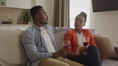 Genç Afrikalı Amerikalı çift oturma odalarında kırmızı şarap içerken sohbet ediyorlar.
