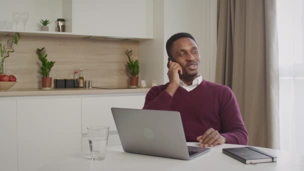 Jovem 20 anos Africano americano preto colega de trabalho falando em um telefone enquanto ele está trabalhando em seu laptop em casa escritório — Vídeo de Stock
